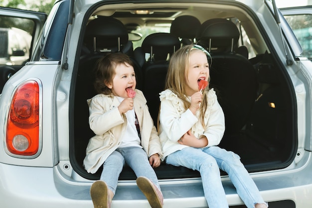 Deux petites filles assises dans le coffre d'une voiture et mangeant des sucettes