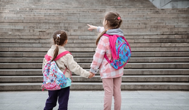 Deux petites filles avec de beaux sacs à dos sur le dos vont à l'école main dans la main. Concept d'amitié d'enfance.