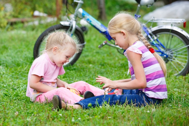 Deux petites filles jouant dans l'herbe avec le ballon contre le vélo