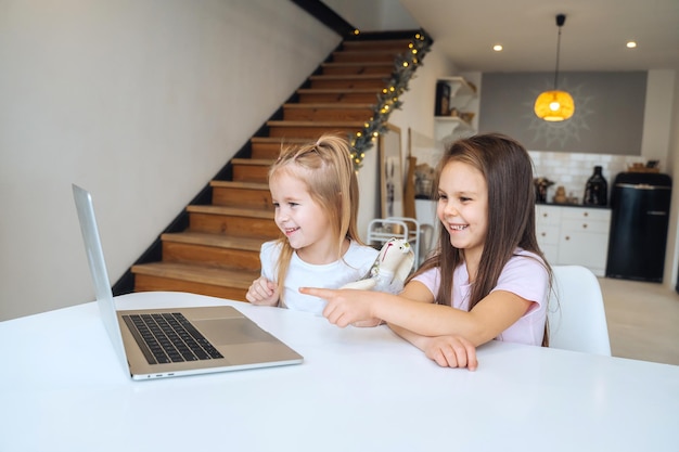 Deux petites filles jouant ensemble à l'ordinateur portable assis à table