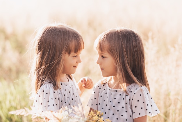 Deux petites filles jumelles identiques heureuses jouant ensemble dans la nature en été. Concept d'amitié et de jeunesse entre filles. Mode de vie des enfants actifs.