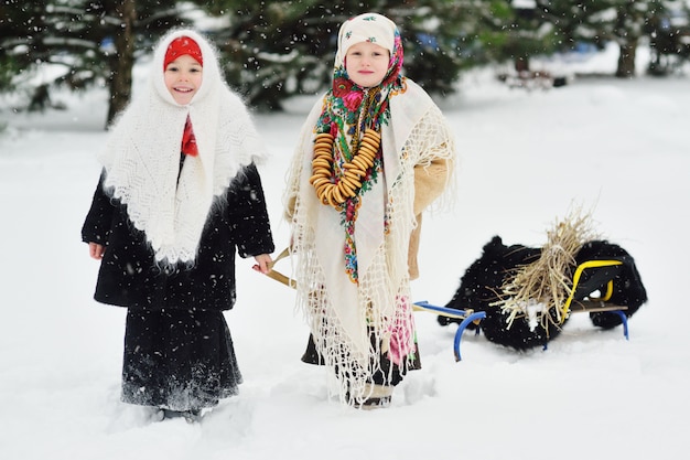 Deux petites filles avec des manteaux de fourrure et des châles dans le style russe sont transportées sur une luge brassée de broussailles