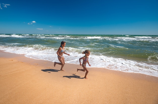 Deux petites filles positives courent le long de la plage de sable par une chaude journée d'été ensoleillée