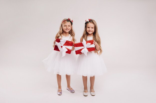 Deux petites filles en robes blanches avec des cadeaux de Noël sur un sourire de fond blanc