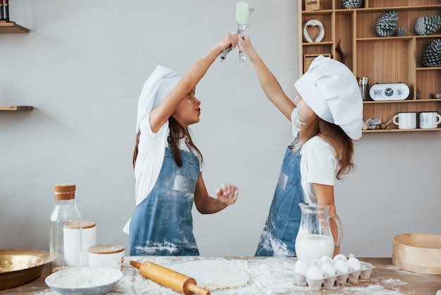 Deux petites filles en uniforme de chef bleu pétrissant la pâte dans la cuisine