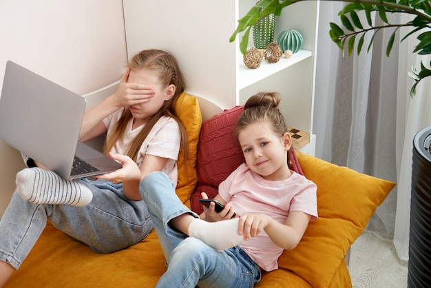 Deux petites soeurs à l'aide d'un ordinateur portable allongé sur le lit à la maison