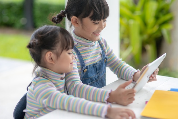 Deux petites soeurs asiatiques jouant avec une tablette numérique à la maison