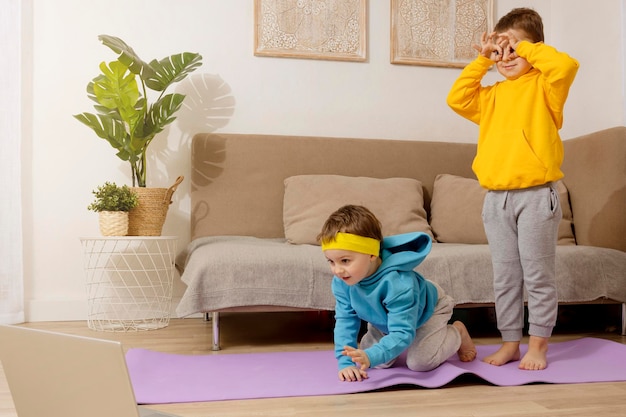 Deux petits enfants caucasiens actifs faisant des exercices de fitness à la maison Relation entre frères Les enfants passent du temps ensemble à s'amuser pendant le sport Les garçons s'entraînent en regardant l'ordinateur