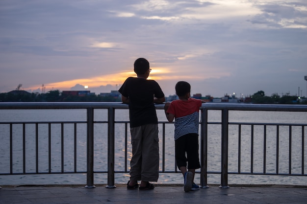 Deux petits enfants debout, regardant la mer au coucher du soleil