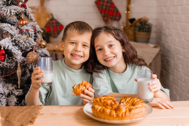 Deux petits enfants un garçon et une fille mangent un gâteau de Noël avec du lait le matin à la maison dans la cuisine