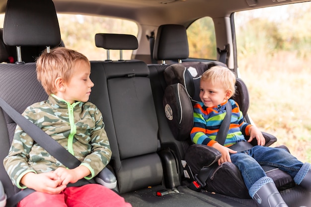 Deux petits garçons assis sur un siège d'auto et un siège d'appoint se sont attachés dans la voiture.