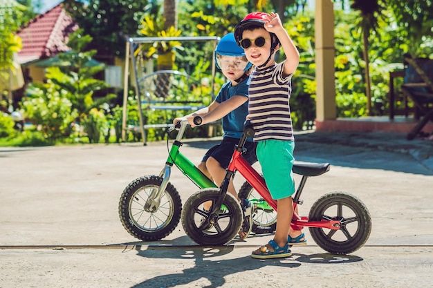 Deux petits garçons enfants s'amusant sur Balance Bike sur une route tropicale de campagne.