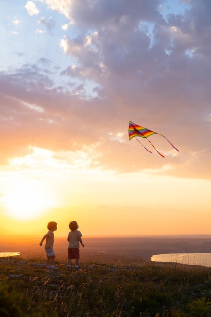 deux petits garçons heureux s'amusant avec le cerf-volant dans la nature au coucher du soleil