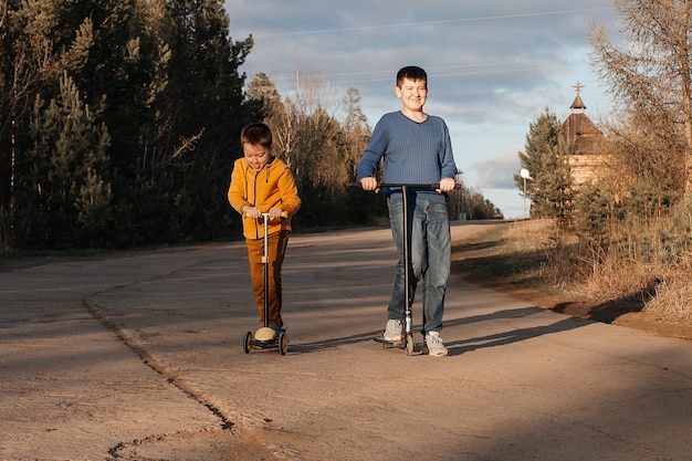 Deux petits garçons montent sur des scooters. Une chaude journée d'été ou de printemps. Les frères s'amusent ensemble. Le concept d'amitié.