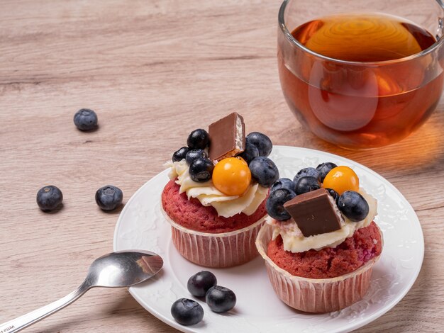 Deux petits gâteaux aux fruits faits maison avec du chocolat sur une assiette blanche, une tasse de thé ronde sur une table en bois. Petit déjeuner à la maison.