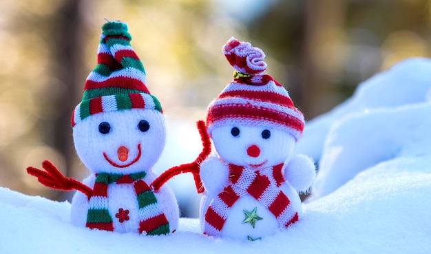 Photo deux petits jouets amusants bébé bonhomme de neige en bonnets et écharpes tricotés dans la neige profonde à l'extérieur sur fond d'espace de copie bleu et blanc vif. carte de voeux de bonne année et joyeux noël.