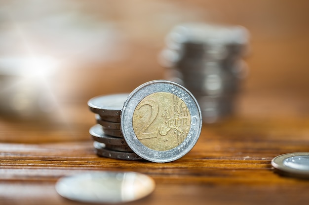 Deux pièces en euros debout près de la pile d'argent disposées en colonne sur une table en bois brun de close up