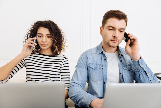 Deux pigistes. Personne de sexe masculin sérieux soulevant les sourcils tout en parlant par téléphone et en regardant des ordinateurs