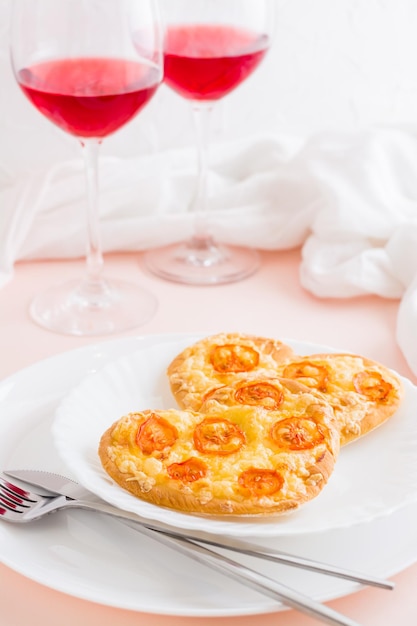 Deux pizzas prêtes à manger en forme de coeur sur des assiettes et des verres de vin sur une table dressée pour la célébration de la Saint-Valentin. Vue verticale