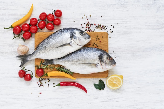 Deux poissons dorada crus avec des légumes sur une planche à découper en bois. Concept de nourriture saine. Vue de dessus, copie