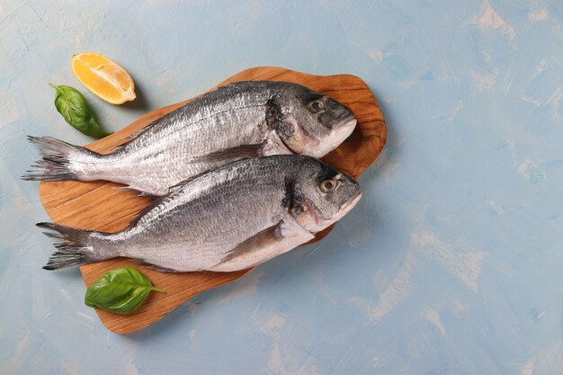 Deux poissons dorado crus au basilic et citron sur planche de bois