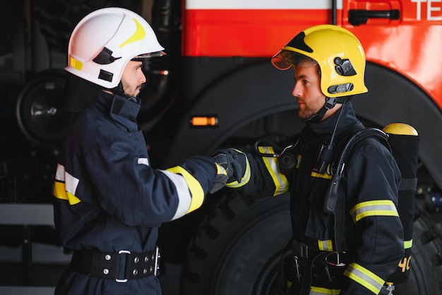 Deux pompiers portant des vêtements de protection dans des casques avec une poignée de main conviviale pour les pompiers