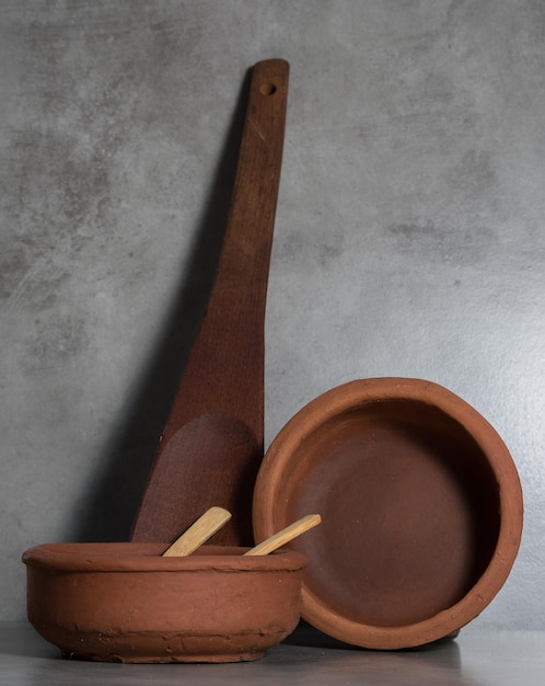 Deux pots en argile rustique grande louche en bois et petites cuillères en bois le tout sur fond gris