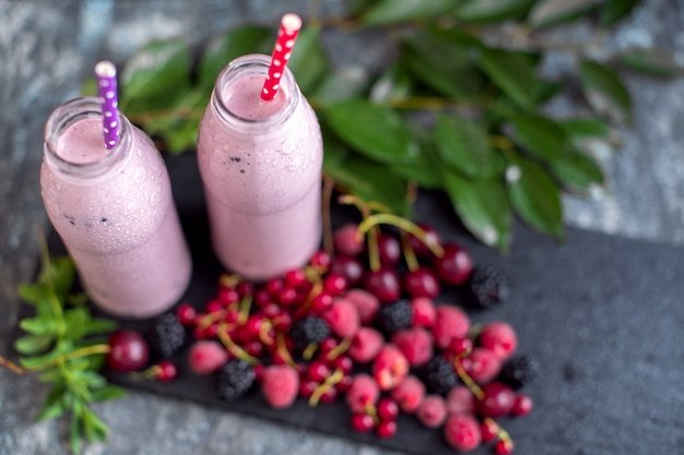 Deux pots de milk-shake ou smoothie avec canneberges, fraises et bleuets debout sur une surface en pierre