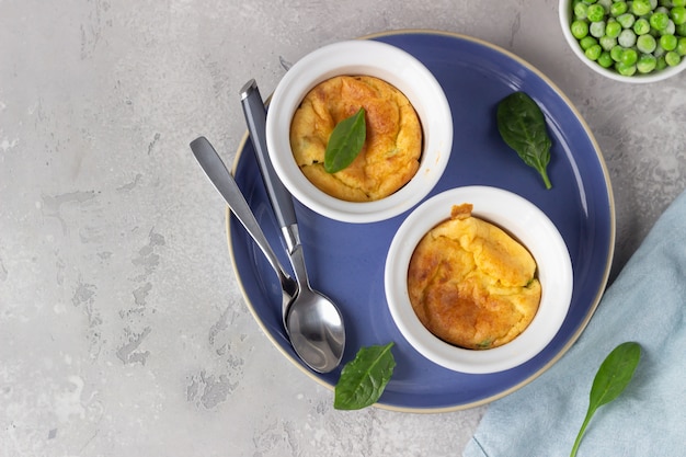 Photo deux ramequins en céramique blanche avec soufflé au fromage au four avec des pois verts sur une table gris clair