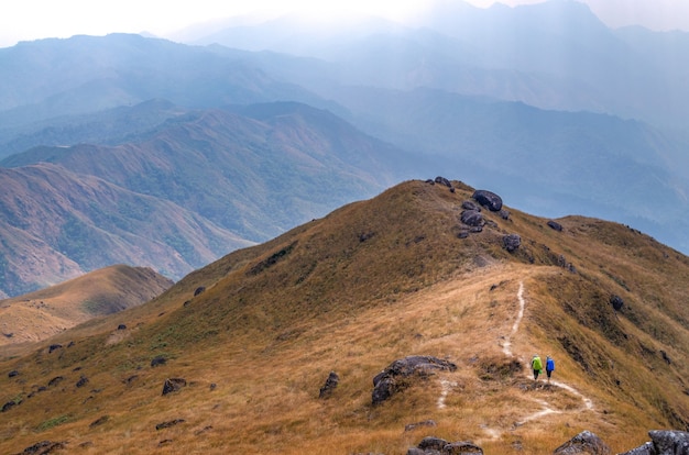 Deux randonneurs marchent sur une chaîne de montagnes à travers des champs dorés à la pagode Muleit, Myanmar (Birmanie).