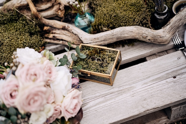 Deux robes de mariée avec une boîte à bijoux en miroir sur des planches en bois avec un bouquet de roses roses