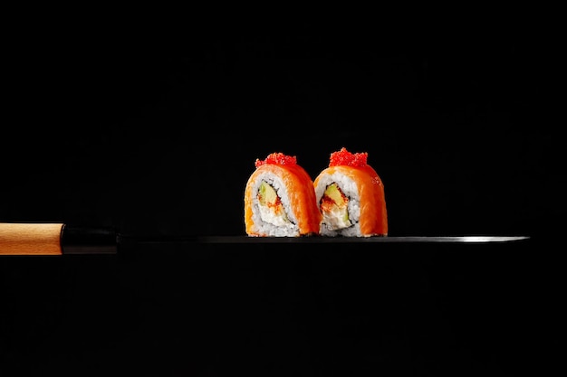 Deux rouleaux de philadelphie avec avocat au fromage à la crème saumon fumé et tobiko sur lame de couteau à sashimi