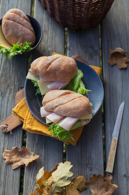 Photo deux sandwichs baguette ciabatta frais avec jambon, fromage et laitue sur fond de bois rustique