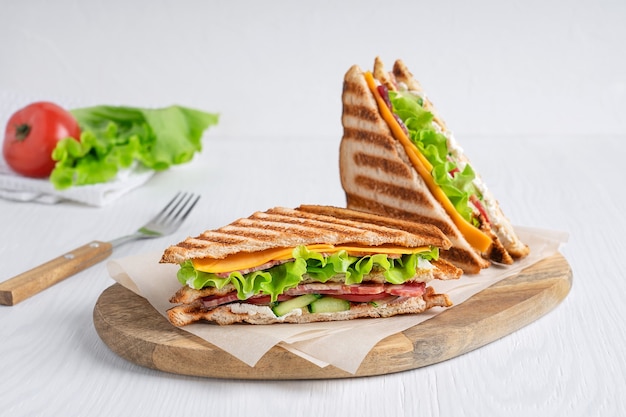 Deux sandwichs faits maison de laitue de fromage de jambon et de pain grillé avec le couteau sur la table en bois blanche