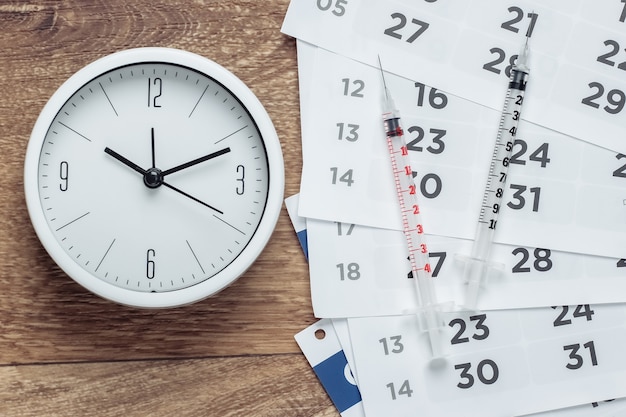 Deux seringues et horloge avec calendrier mensuel sur plancher en bois. Vaccination