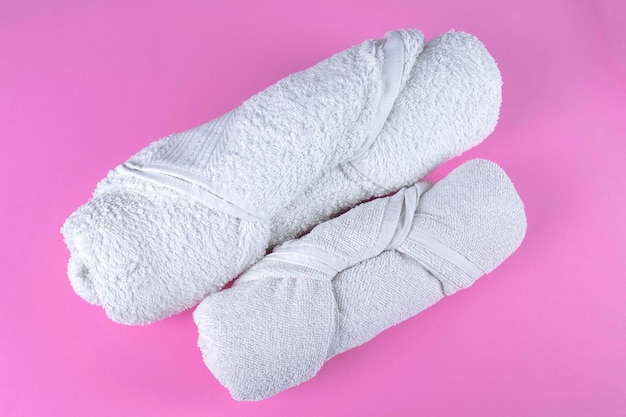 Deux serviettes de bain blanches roulées pliées sur fond rose