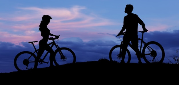 Deux silhouettes de cyclistes sur fond de coucher de soleil Un gars athlétique et une fille sur des vélos de montagne modernes