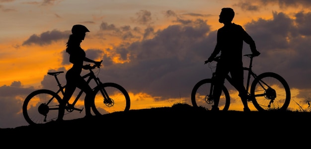 Deux silhouettes de cyclistes sur fond de coucher de soleil Un homme sportif et une fille sur des vélos de montagne modernes vont l'un à l'autre