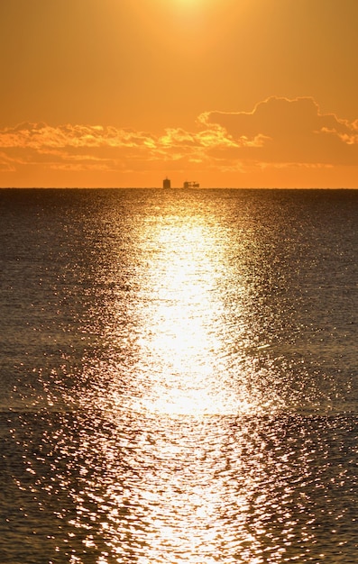 Deux silhouettes d'un pétrolier sur la ligne d'horizon dans la mer et un chemin ensoleillé à la surface de la se