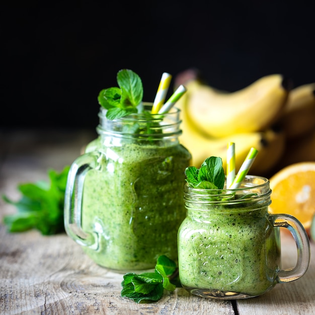 Deux smoothies verts sains aux épinards, banane, orange et menthe dans un bocal en verre et ingrédients. Détox, alimentation, concept de nourriture saine et végétarienne.