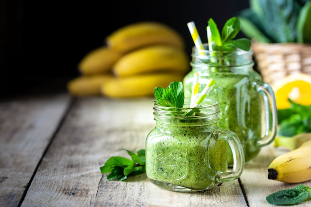 Deux smoothies verts sains aux épinards, banane, orange et menthe dans un bocal en verre et ingrédients