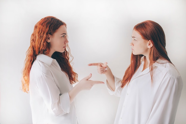 Deux sœurs aux cheveux roux sont isolées sur fond blanc dans des chemises surdimensionnées spacieuses. DEUX jeunes filles s'accusent mutuellement de leurs actes.