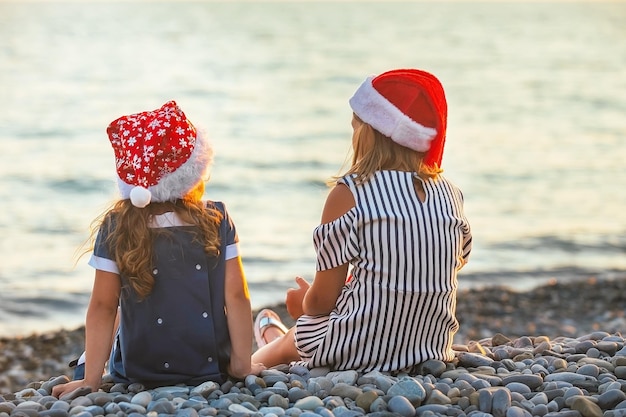 Deux soeurs en chapeaux de père noël s'asseoir et discuter joyeusement au bord de la mer au coucher du soleil