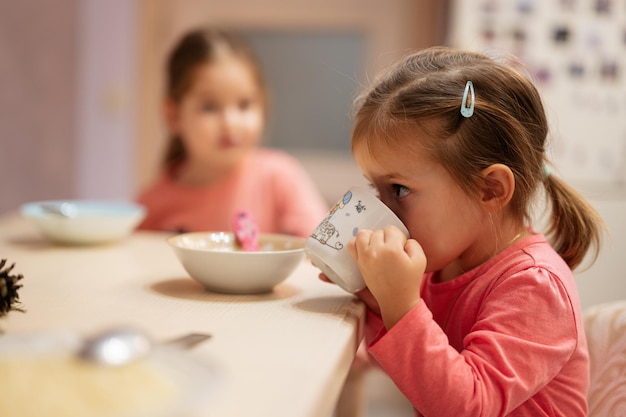 Deux sœurs dînent ensemble dans la cuisine petite fille boit dans une tasse