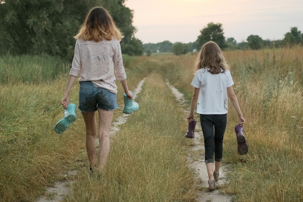 Deux sœurs de filles heureuse marchant avec des bottes de pluie dans les mains