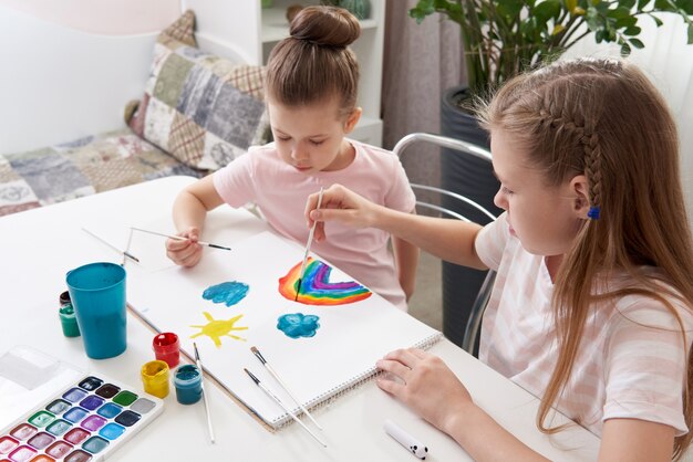 Deux soeurs heureuses peignant à la maison, dessin arc-en-ciel