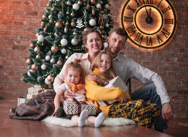 Deux sœurs et leurs parents assis près de l'arbre de Noël