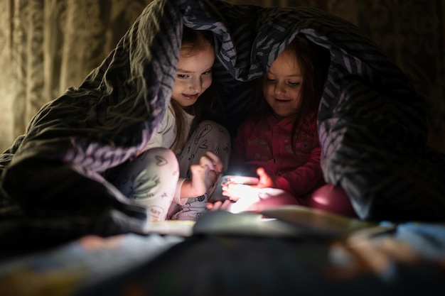 Deux sœurs regardant un film ou un dessin animé sur un smartphone avec une couverture au lit la nuit à la maison