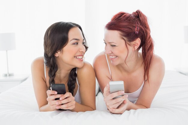 Deux souriant amis femmes SMS sur le lit