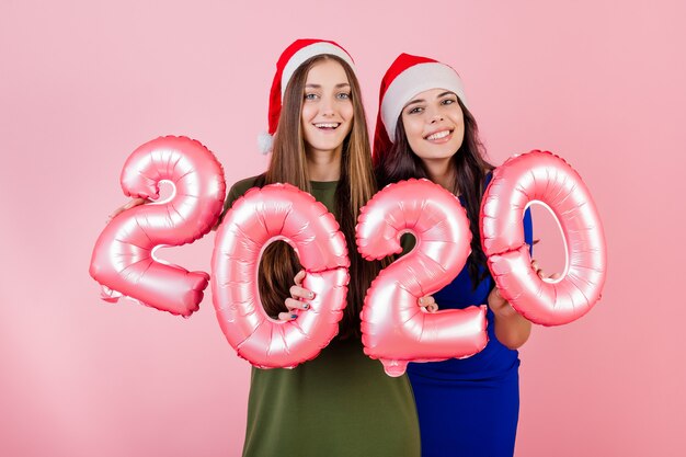 Deux, sourire, femmes, porter, chapeaux santa, tenue, 2020, ballons, pour, nouvel an, vacances, sur, rose